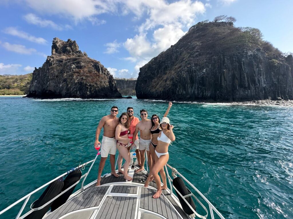 Lancha navegando pelas águas cristalinas de Noronha com Morro Dois Irmãos ao fundo